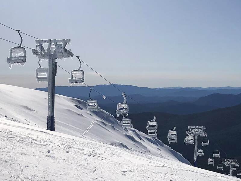 Empty chairlift chairs encrusted in rime ice on a clear morning, the ranges stretching away behind.