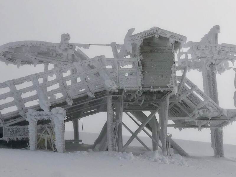 A lift structure completely encased in wind-driven rime ice, sculptural against flat white cloud.