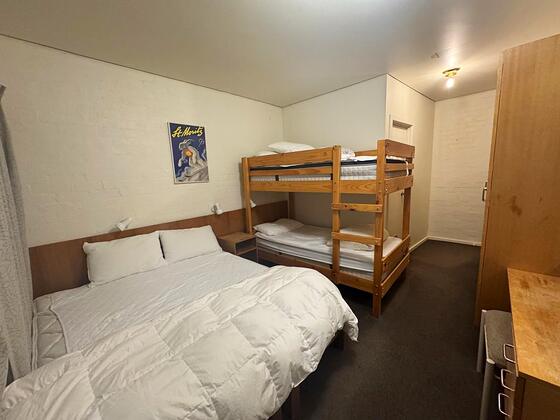 Room 1: queen bed at left, a single-over-single bunk at right, wardrobe and a framed ski poster.
