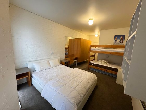 Room 12: queen bed at left, a single-over-single bunk at right, timber wardrobe, desk and a framed ski poster.