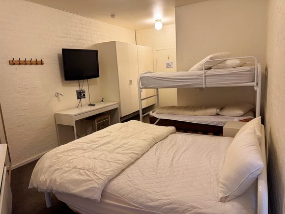 Room 13: queen bed with a white single-over-single bunk beside it, a wall-mounted television, desk and wardrobe.
